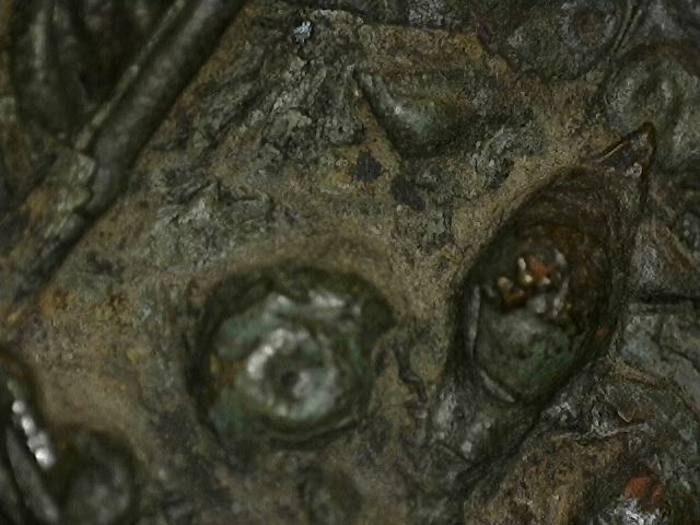 Mikroskopische Makroaufnahme der natürlichen Alterungspatina einer antiken thailändischen Bronzefigur. Sichtbar sind komplexe Korrosionsschichten aus rötlichem Cuprit, grünem Malachit und tiefblauen Azurit-Kristallen auf der ziselierten Oberfläche. Ein authentisches Zeugnis jahrhundertealter Oxidation.